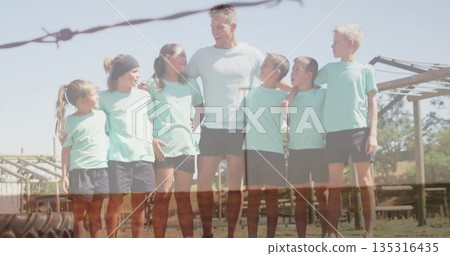 Huddling coach and team linking shoulders on dusty training field, with monkey bars, barbed fence 135316435
