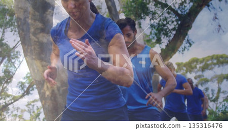 Running woman in blue shirt leaning along tree-lined grassy trail, with training group, copy space 135316476