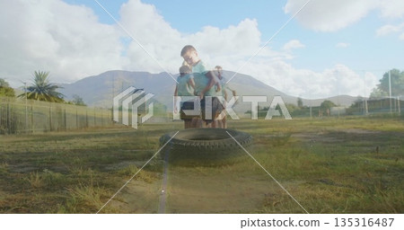 Pulling tire by chain, boy wearing light blue polo and navy shorts exercising on school field Pulling tire by chain, boy wearing light blue polo and navy shorts exercising on school field 135316487