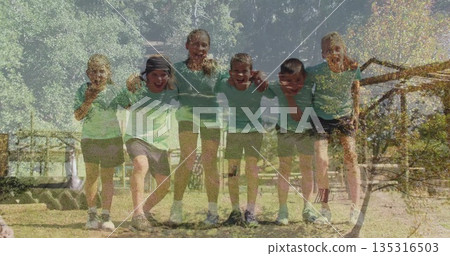 Six children wearing green tshirts linking arms, smiling on grassy park field with wooden fence 135316503