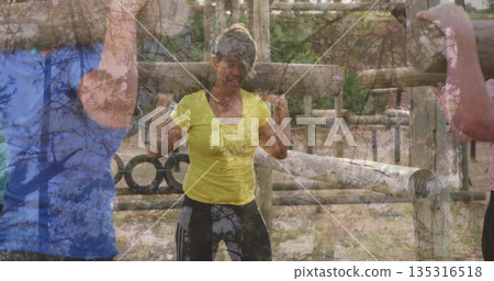 Leading mature woman guiding group workout around wooden obstacle forest clearing, with metal rings 135316518