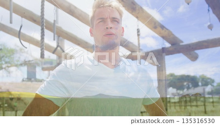 Gazing athlete wearing white T-shirt under wooden horizontal bars in park with gymnastic rings 135316530