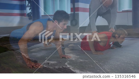 Trainer guiding clients in gear doing push-ups in gym, with mats, straps, rack and bag frame 135316546