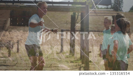 Leading fitness coach instructing five children on wooden obstacle course in field, with whistle Leading fitness coach instructing five children on wooden obstacle course in field, with whistle 135316554