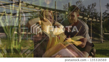 Performing sit-ups woman wearing workout clothes on grass beneath wooden bars, trainer guiding 135316569