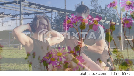 Performing abdominal crunches pair in sportswear at park with mat bars smartwatch and daisy overlay Performing abdominal crunches pair in sportswear at park with mat bars smartwatch and daisy overlay 135316582