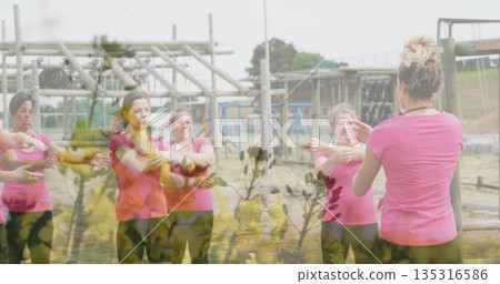 Stretching women in matching pink tops and black leggings following leader at obstacle course beams Stretching women in matching pink tops and black leggings following leader at obstacle course beams 135316586