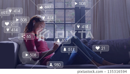 Relaxing woman reclining on cushioned sofa using earbuds, tablet in living room, social media icons 135316594