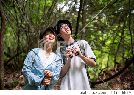 Asian tourist woman man friends or couple standing looking up while hiking or trekking in a forest. 135316639