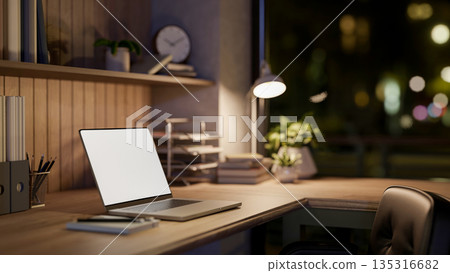 White screen laptop and book under lamp light on wooden table in dim room or office. Work or Study. White screen laptop and book under lamp light on wooden table in dim room or office. Work or Study. 135316682