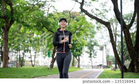 Young asian woman in sportswear with headphones on running or jogging to exercise or workout in park Young asian woman in sportswear with headphones on running or jogging to exercise or workout in park 135316941