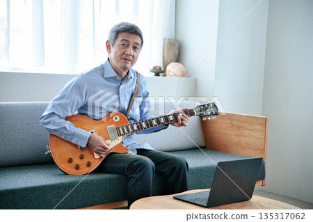 Senior man taking online guitar lessons on laptop 135317062
