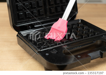 Preparing a black electric waffle maker with oil for baking. Preparing a black electric waffle maker with oil for baking. 135317197