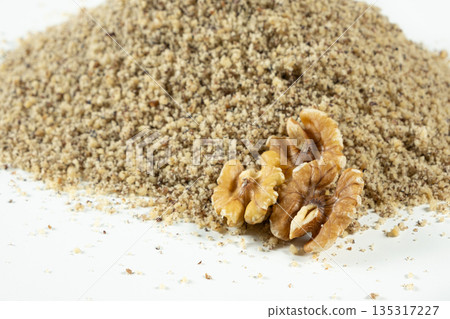 Whole walnut halves on crushed walnut kernels on white background. Whole walnut halves on crushed walnut kernels on white background. 135317227