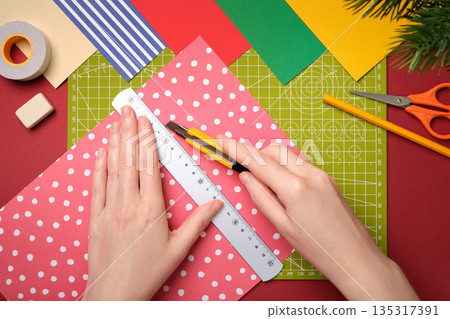 Top view of hands cutting patterned paper with craft knife and ruler on cutting mat. DIY, crafting, handmade projects, and creative hobbies. Top view of hands cutting patterned paper with craft knife and ruler on cutting mat. DIY, crafting, handmade projects, and creative hobbies. 135317391