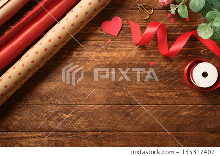Gift wrapping background. Paper with red hearts, ribbon, and scissors on wooden background. Presents preparation. Copy space 135317402