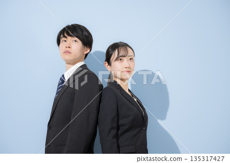 幾位年輕商務人士背對背站在淺藍色背景前。這幅企業招募圖片傳遞出對應屆畢業生招募和就業的信任訊息。 135317427