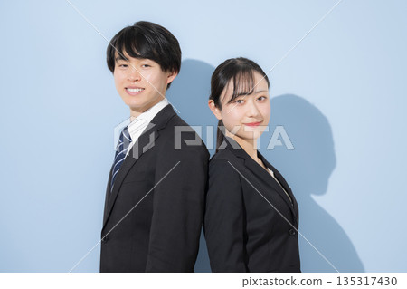一男一女，看起來像是年輕的商人和大學生，背靠背站在淺藍色背景前。 135317430