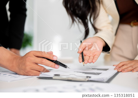 Close up businessman and woman's hand holding pen over document on clipboard at work table in office Close up businessman and woman's hand holding pen over document on clipboard at work table in office 135318051