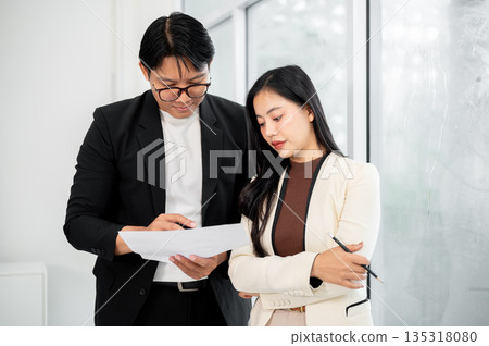 Serious businessman and woman or office worker standing looking intently at the important document. 135318080