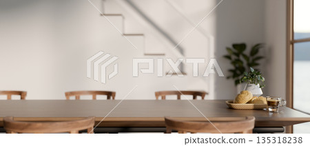 Breads and coffee on wooden dining table and chairs beside stairs in modern house or office building 135318238