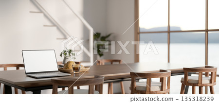 White screen laptop on wood dining table and chairs beside stairs in modern house or office building 135318239