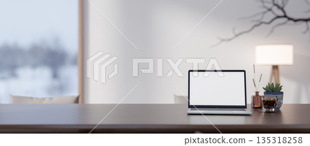 White screen laptop and coffee on wooden table in a room with floor lamp and snow outside glass door White screen laptop and coffee on wooden table in a room with floor lamp and snow outside glass door 135318258