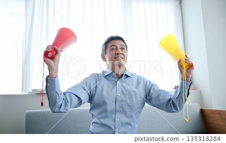 Senior man cheering while watching TV Senior man cheering while watching TV 135318284
