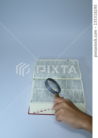A magnifying glass is used to look up information in a dictionary, and there is ample space between the text. A magnifying glass is used to look up information in a dictionary, and there is ample space between the text. 135318295