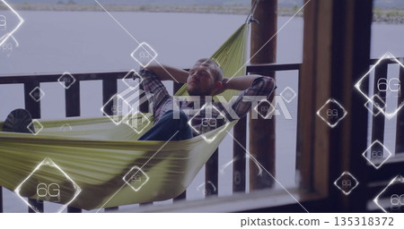 Reclining male in shirt viewing 6G icons on green hammock between wooden posts at lakeside porch Reclining male in shirt viewing 6G icons on green hammock between wooden posts at lakeside porch 135318372