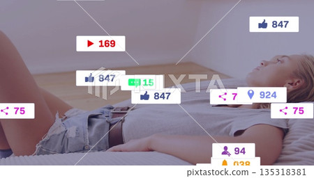 Lying woman wearing grey shirt, denim shorts on bed in bedroom, with social media icons floating 135318381