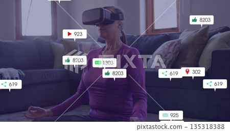 Sitting mature woman wearing VR headset meditating in living room, with floating social media icons Sitting mature woman wearing VR headset meditating in living room, with floating social media icons 135318388