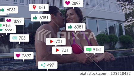 Leaning woman in pink bikini and shirtless man smiling poolside at home with floating digital icons 135318422