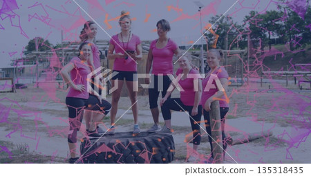 Posing six women in pink athletic tops resting on tractor tire at obstacle course, with stopwatch Posing six women in pink athletic tops resting on tractor tire at obstacle course, with stopwatch 135318435