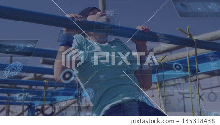 Pulling up boy wearing headband and wristbands on metal bars at obstacle course, yellow rope nets Pulling up boy wearing headband and wristbands on metal bars at obstacle course, yellow rope nets 135318438