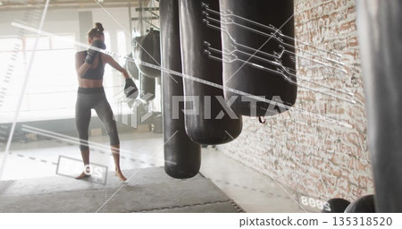 Punching woman wearing boxing gloves and leggings at studio with heavy punching bags, copy space 135318520