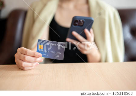 Close up woman's hand holding phone and showing credit card while sitting on leather sofa in cafe. 135318563