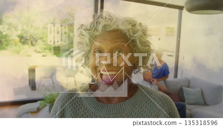 Smiling senior woman wearing gray sweater sitting on sofa in living room, with floating data charts 135318596