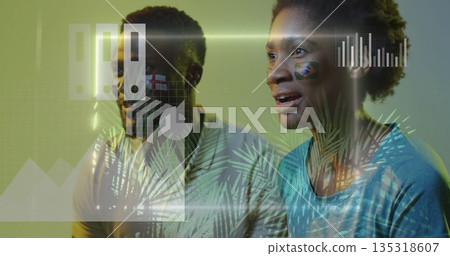 Watching woman and man reacting in living room, with face-painted national flags and chart overlays 135318607