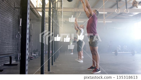 Man in burgundy holding medicine ball overhead at functional gym, with rig, barbells, copy space Man in burgundy holding medicine ball overhead at functional gym, with rig, barbells, copy space 135318613