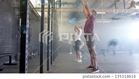 Holding medicine ball overhead, man in purple T-shirt performing overhead throw at CrossFit gym Holding medicine ball overhead, man in purple T-shirt performing overhead throw at CrossFit gym 135318618