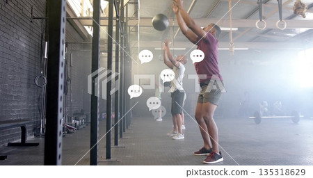 Slamming man in maroon shirt throwing medicine ball against brick wall with squat racks, copy space Slamming man in maroon shirt throwing medicine ball against brick wall with squat racks, copy space 135318629