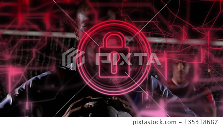 Athlete in soccer jersey holding soccer ball before goal net at night, with digital padlock overlay Athlete in soccer jersey holding soccer ball before goal net at night, with digital padlock overlay 135318687