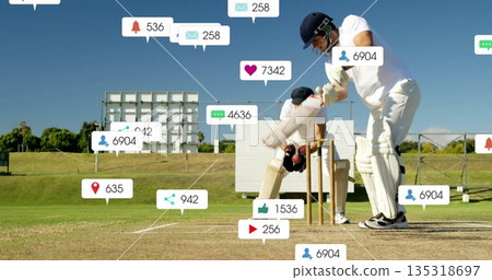 Swinging batsman holding cricket bat facing floating social media icons on grassy field, copy space 135318697