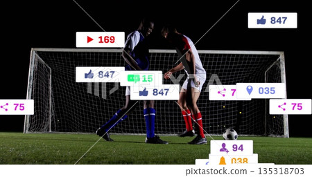 Players wearing blue-red kits racing for ball on pitch at night, with goal net and overlays 135318703