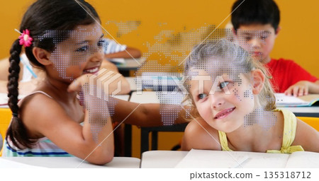 Smiling two girls leaning together and conversing in school classroom, with notebooks and pencils 135318712