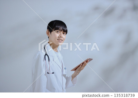 A young male doctor in a white coat holding a tablet 135318739