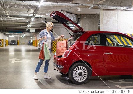 A woman loads shopping bags into the trunk of a red car in an underground parking garage A woman loads shopping bags into the trunk of a red car in an underground parking garage 135318766