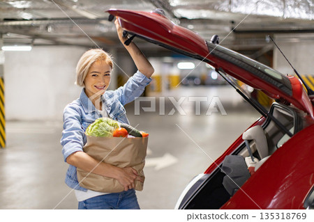 A smiling woman loads groceries into the trunk of her car in a parking garage A smiling woman loads groceries into the trunk of her car in a parking garage 135318769