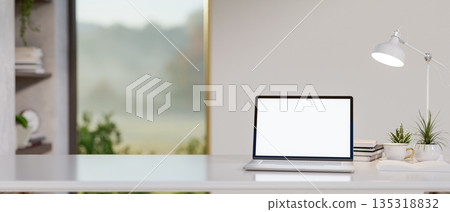 White screen laptop with coffee or tea cup under lamp light on shiny table in a glass door room. 135318832